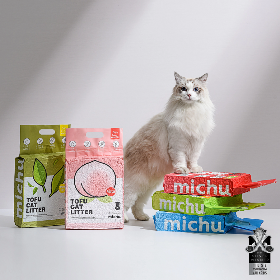Cat sitting on a stack of Michu tofu cat litter packages with a white background